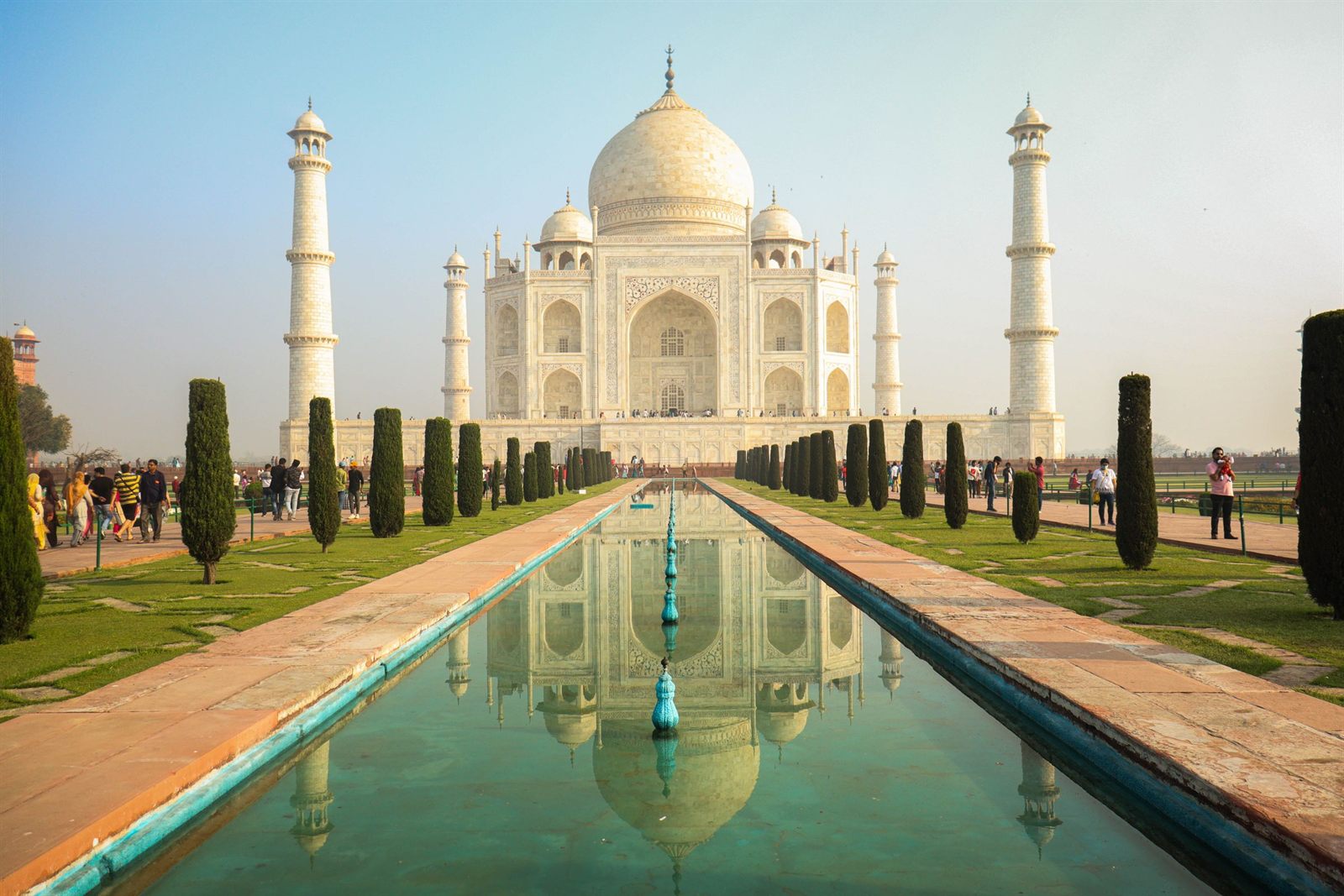 The Taj Mahal reflected in its long garden pool, with visitors walking the paths